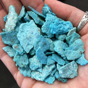 A pile of bright blue Turquoise chips in the palm of a hand