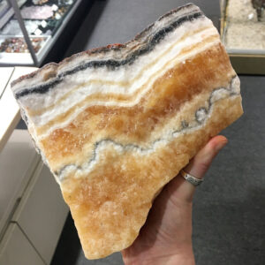 A hand holding a 6.88 pound piece of Honey Band Calcite rough rock. The rock is wet to bring out the color.