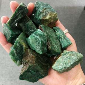 A hand holding a pile of ten pieces of green Aventurine rough rock, pictured wet.