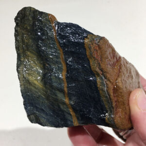 0.60 pound piece of Blue Tiger Eye rough rock, pictured wet. Side one of six sides.