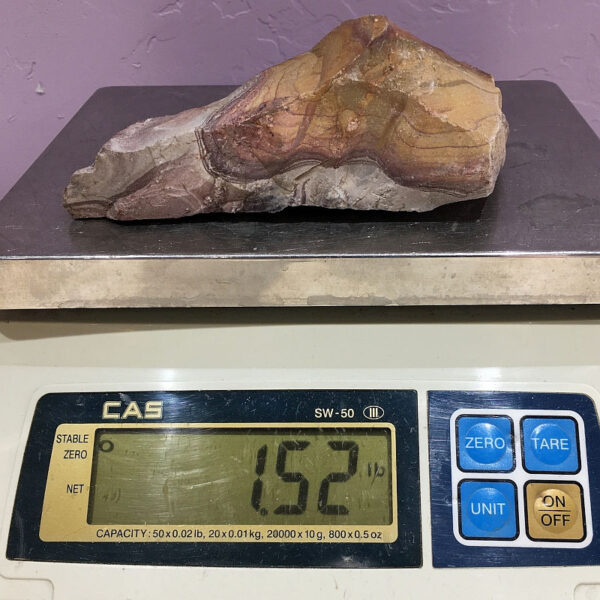 A piece of Mexican Rhyolite rough rock pictured on a scale. Piece weighs 1.52 pounds.