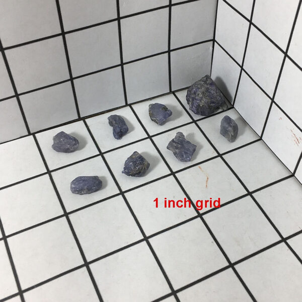 Eights pieces of Tanzanite rough rock pictured on a one inch grid. Piece measures approximately 0.25 to 0.75 inches each