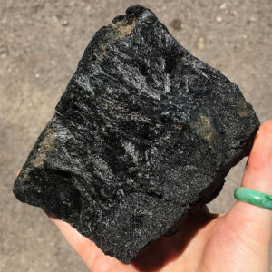 3.08 pound piece of Velvet Black Tourmaline rough rock pictured in sunlight. Side one of six sides.