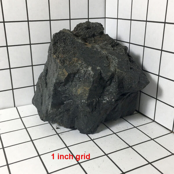 3.08 pound piece of Velvet Black Tourmaline rough rock pictured on a one inch grid. Piece measures approximately 4.5 by 3.5 by 4 inches.