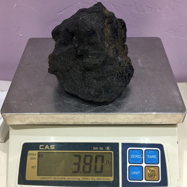 A piece of Velvet Black Tourmaline rough rock pictured on a scale. Piece weighs 3.80 pounds.