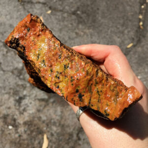 2.98 pound piece of Flash Jasper (Tiger Tail) rough rock. Pictured wet, in sunlight. Side one of six sides.