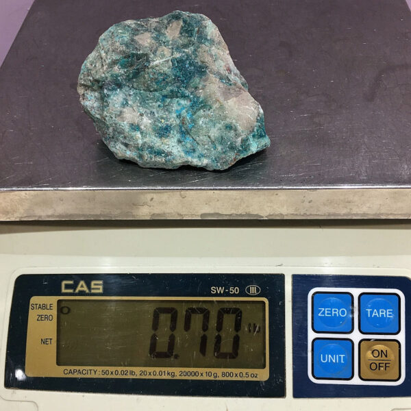 A piece of Teal Turq Rhyolite rough rock pictured on a scale. Piece weighs 0.70 pounds.