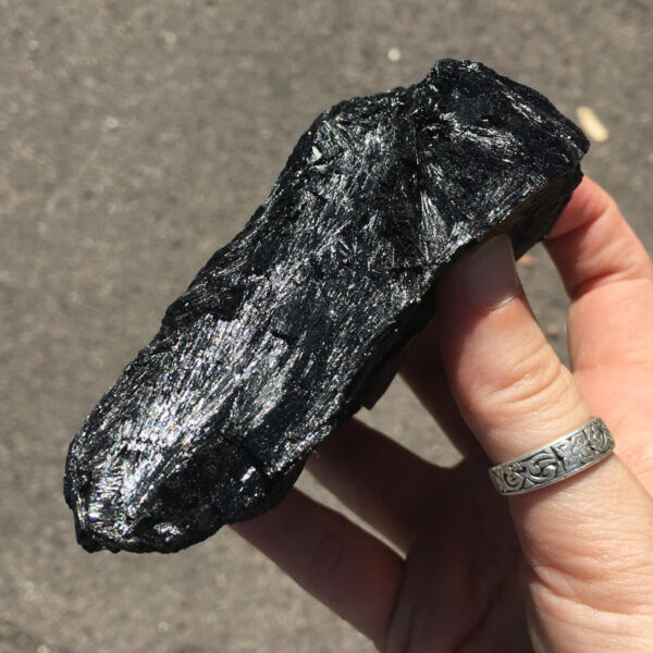 1.56 pound piece of Velvet Black Tourmaline rough rock, pictured dry in sunlight. Side three of six sides.