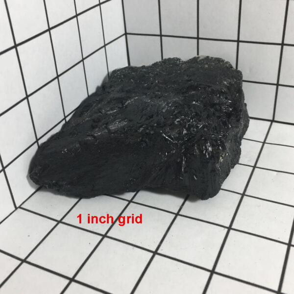 1.56 pound piece of Velvet Black Tourmaline rough rock pictured on a one inch grid. Piece measures approximately 4.5 by 3.5 by 1.75 inches