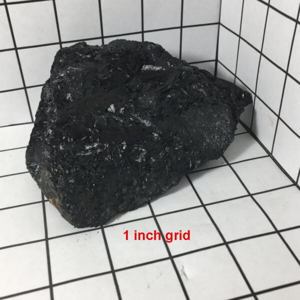 1.70 pound piece of Velvet Black Tourmaline rough rock pictured on a one inch grid. Piece measures approximately 5.25 by 4 by 2 inches