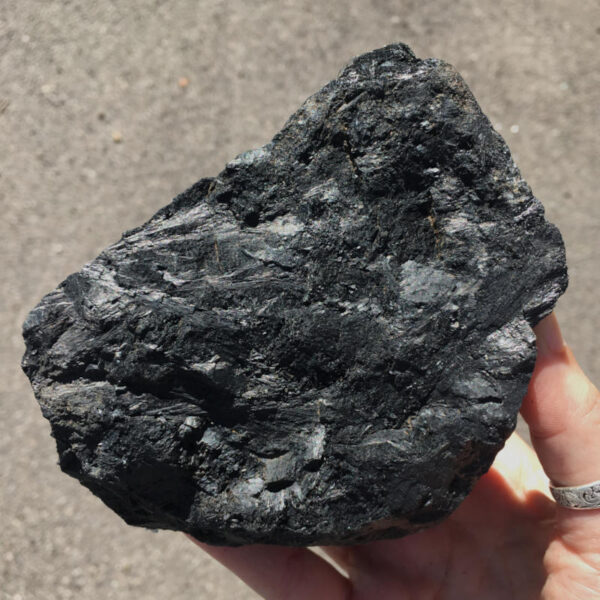 2.04 pound piece of Velvet Black Tourmaline rough rock, pictured dry in the sunlight. Side three of six sides.