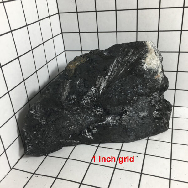 5.22 pound piece of Velvet Black Tourmaline rough rock pictured on a one inch grid. Piece measures approximately 5.25 by 6 by 3.75 inches